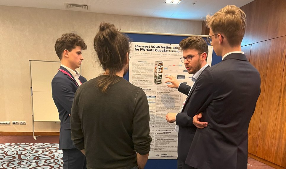 Photo of four people standing by a poster