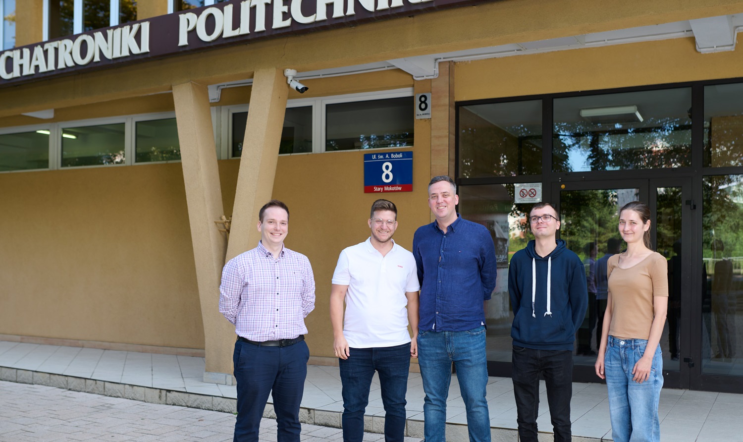 Photo of Professor Maciej Trusiak with members of the research team in front of the building of the Faculty of Mechatronics