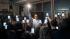 In the photo: a man is holding a lit light bulb, and a group of people are holding mobile phones
