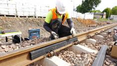 A man wearing a helmet and a reflective vest is working on the railway tracks