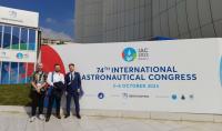 Photo of three students at the information board about the 74th International Astronautical Congress